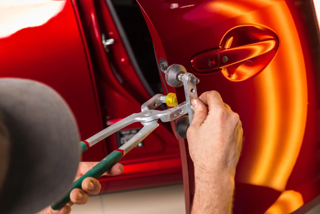 Professional paintless dent repair technician working on car door at auto body shop